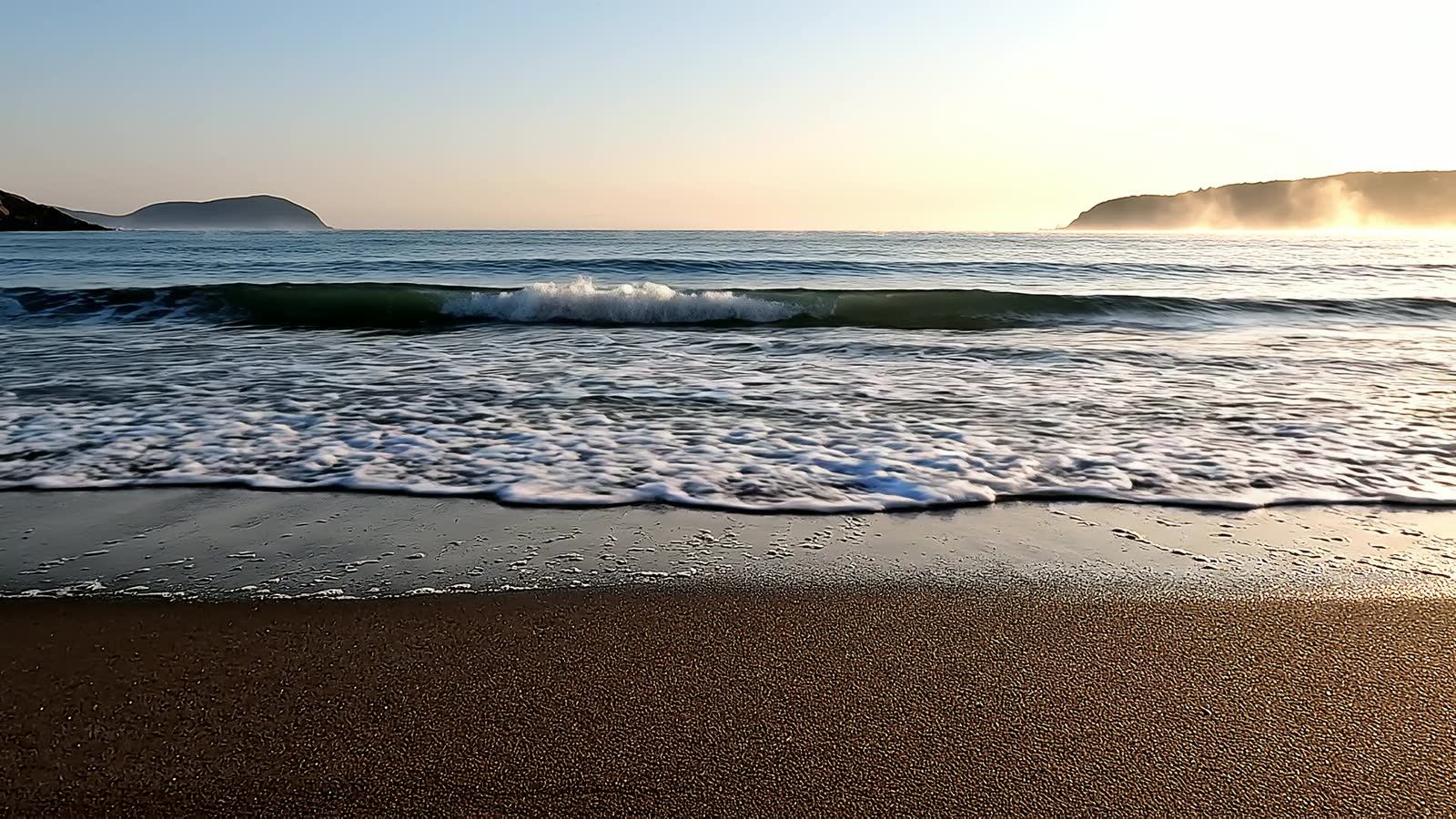 Gentle waves reaching a quiet shoreline at sunrise